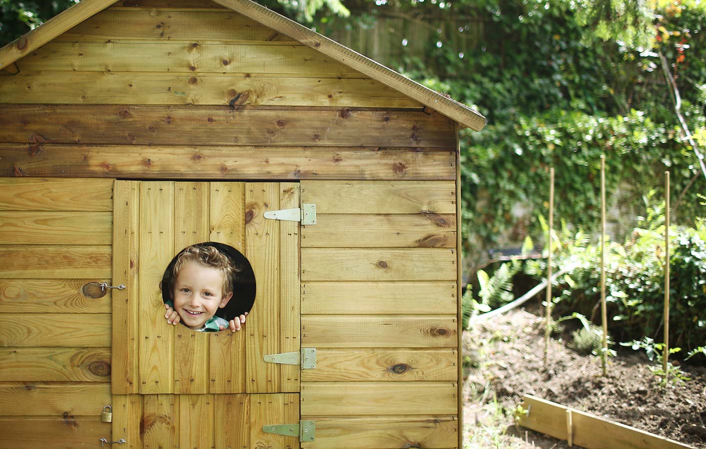 Gartenholz in einem Gartenspielhaus für Kinder, Junge schaut aus dem Fenster.